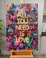 Colorful artwork with 'All You Need Is Love' text on a stand.